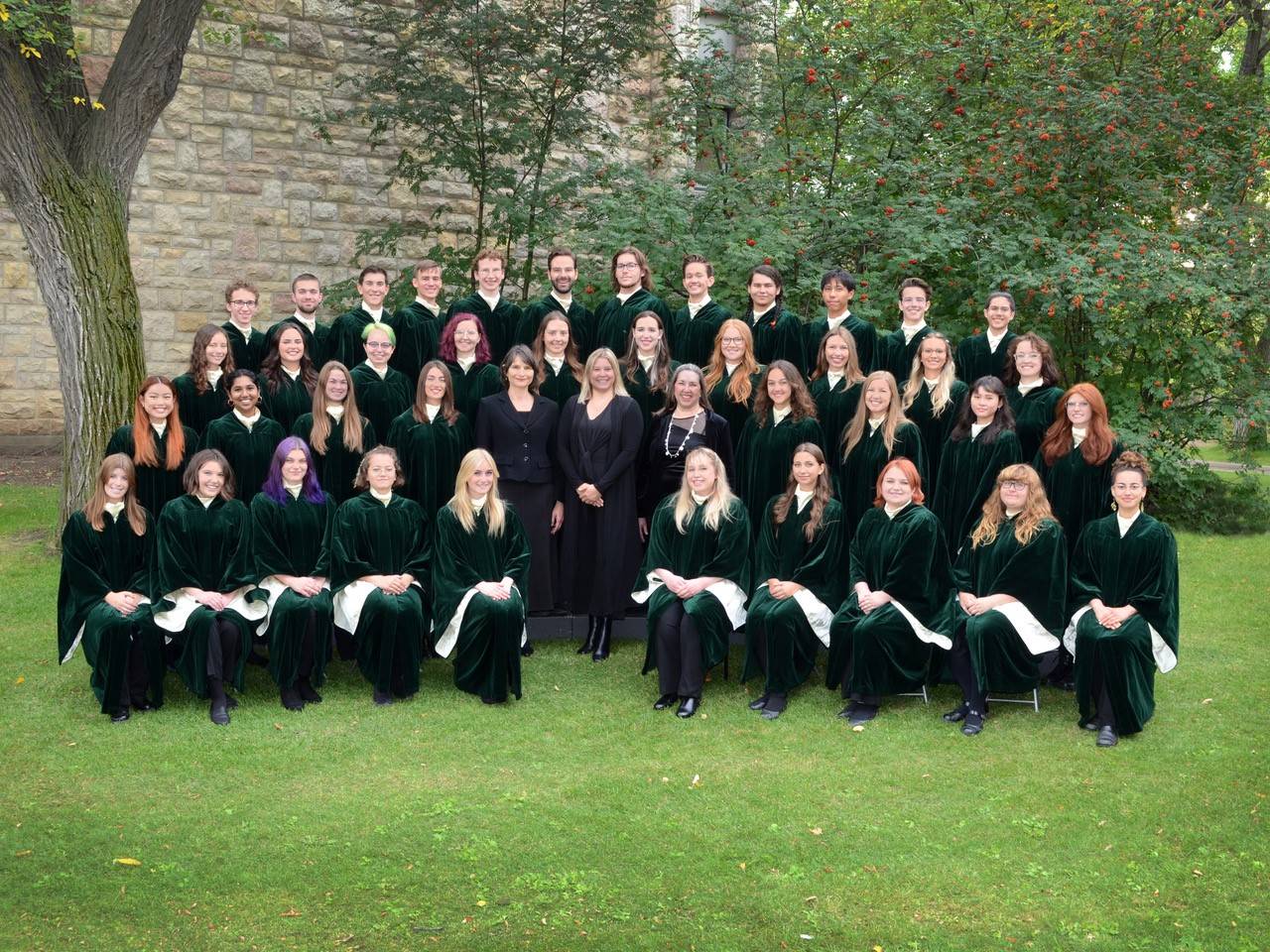 A group of people wearing dark green robes seated in choir formation