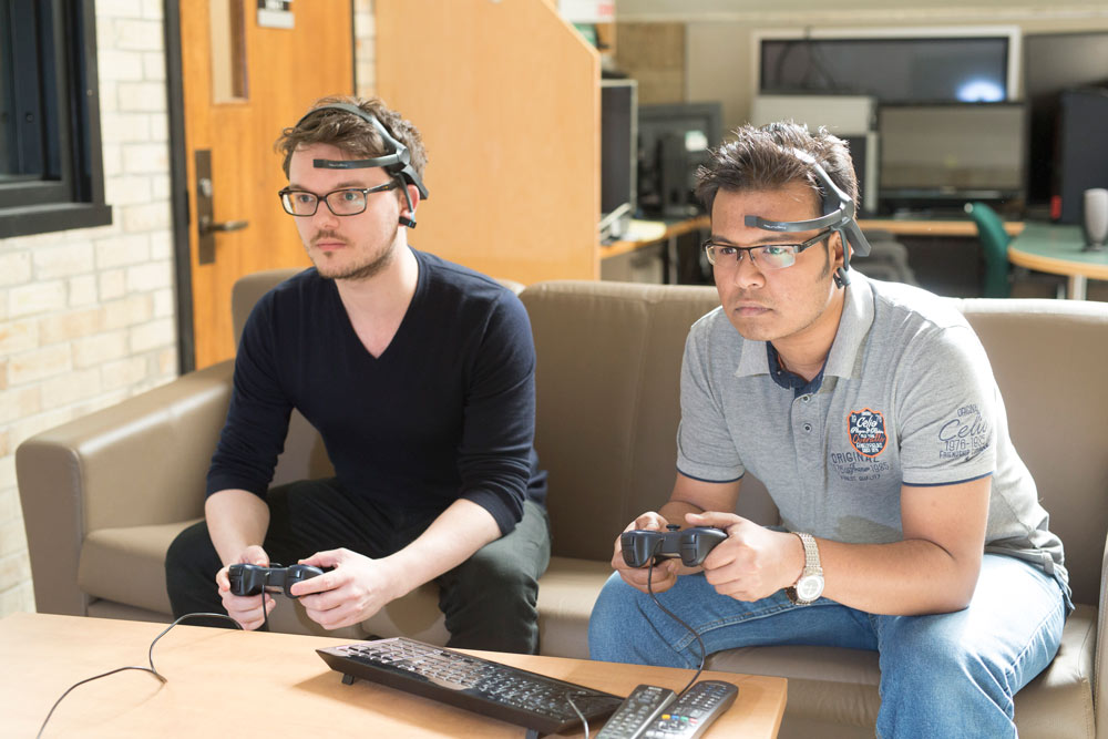 Students Ansgar Depping and Rasam Bin Hossain wear brainwave-sensing headsets while gaming: one of the ways emotional states are measured in the HCI lab.