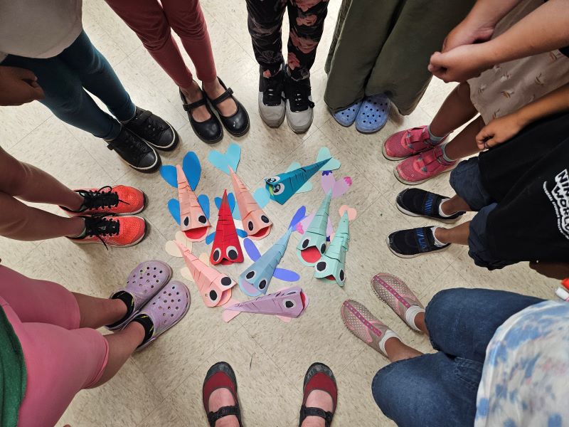 children's feet in a circle with paper fishcrafts in the middle